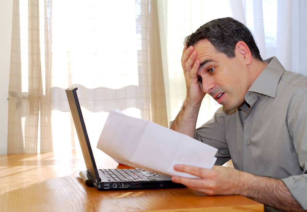 Frustrated man looking at paper, open laptop